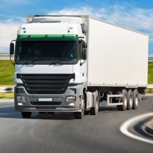 White truck driving around a corner with a background of green grass