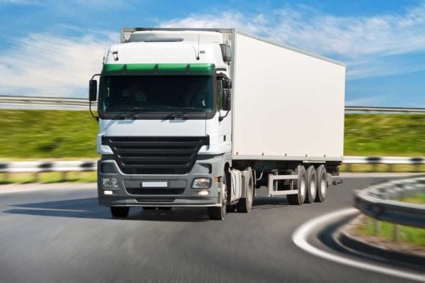 White truck driving around a corner with a background of green grass