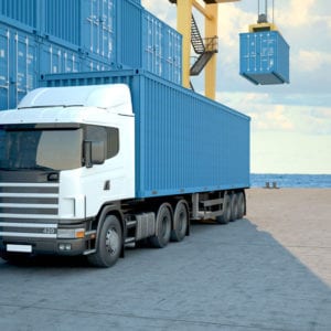 Blue Truck in front of a row of blue shipping containers with the ocean in the background
