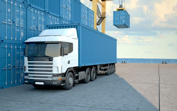 Blue Truck in front of a row of blue shipping containers with the ocean in the background